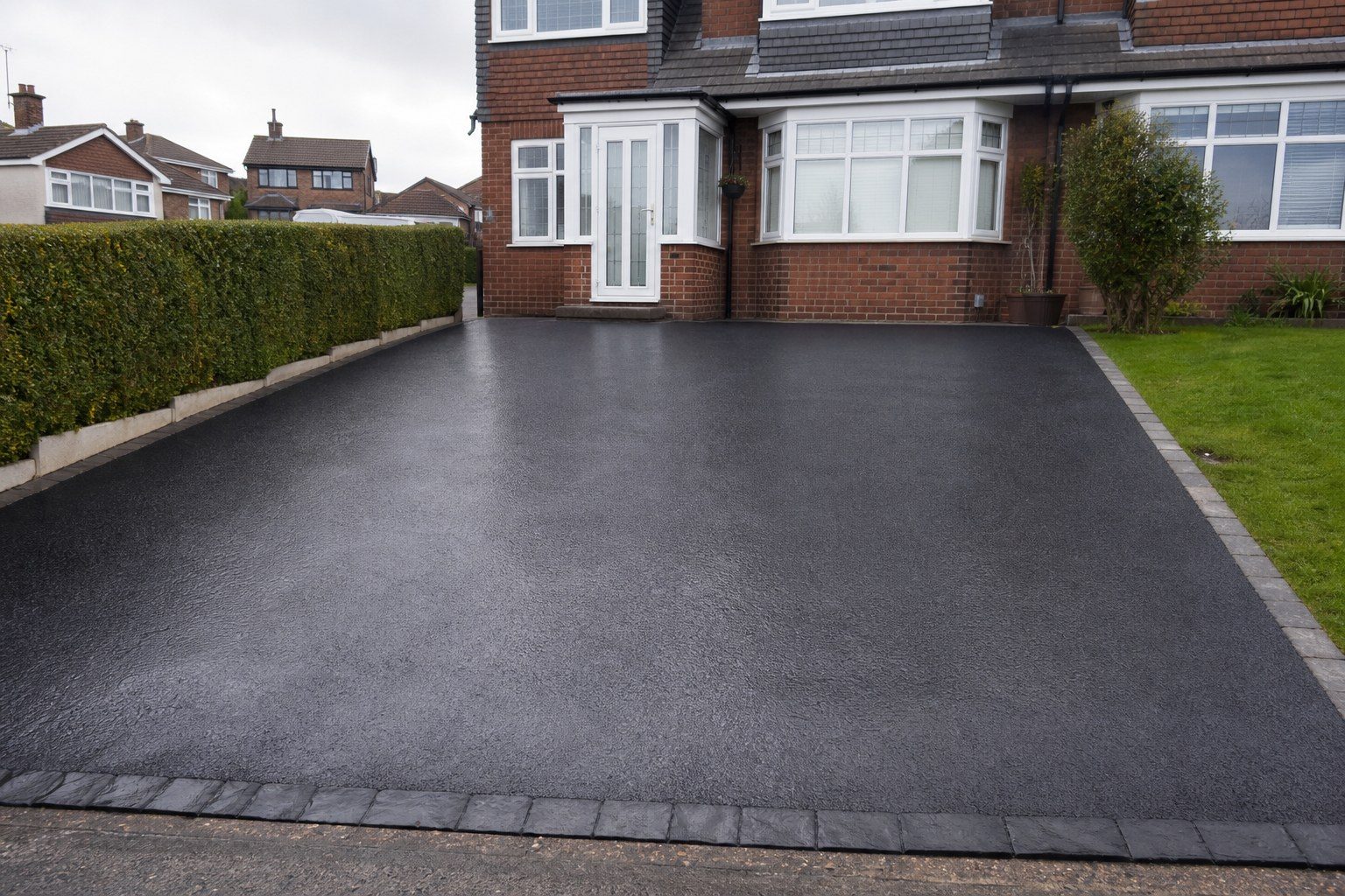 Freshly cleaned black tarmac driveway in front of a brick semi
